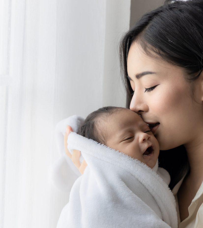 Portrait of asian young mother kissing her cute newborn baby in Portrait of asian young mother kissing her cute newborn baby in white bed room. Wife and mother's day concept.