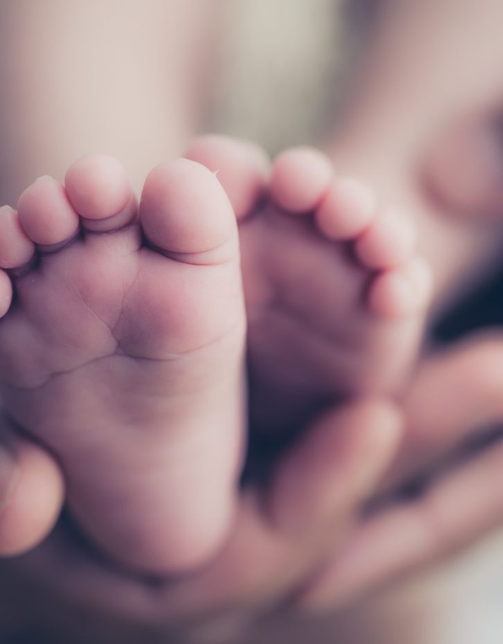 Feet of a newborn baby in the hands of parents. Happy Family onc Feet of a newborn baby in the hands of parents. Happy Family oncept. Mum and Dad hug their baby's legs.